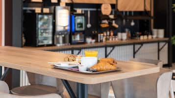 A breakfast tray with croissants, a cup of coffee, and a glass of orange juice on a wooden table in a cafe setting.