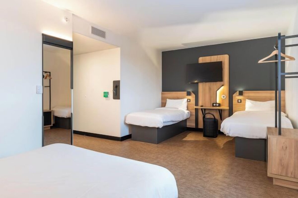 A hotel room with two beds, a wooden headboard, a small desk, and a hanging coat rack.
