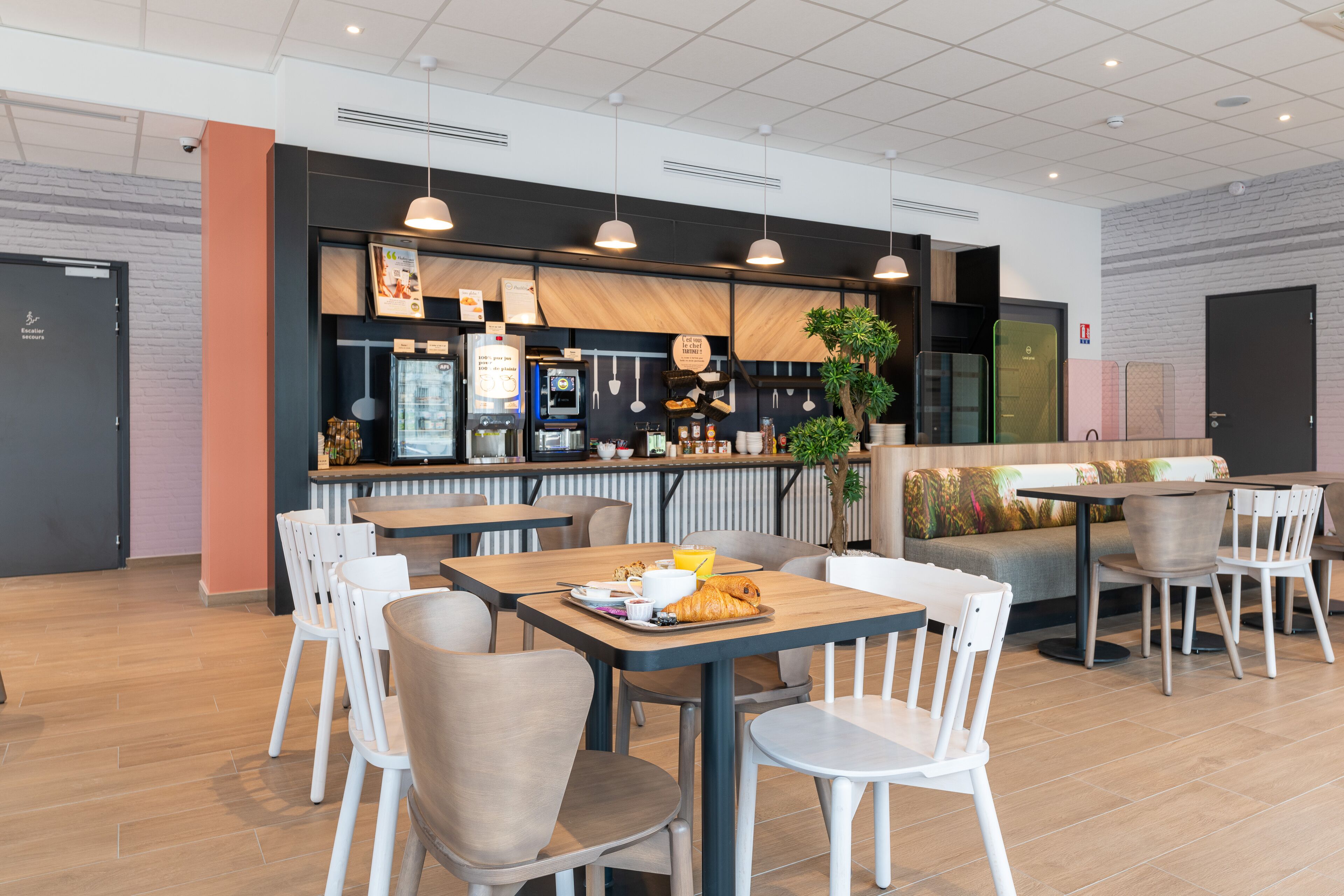 Un café moderne doté de plusieurs espaces de détente, comprenant des tables et des chaises, ainsi qu’un comptoir avec une machine à café et un menu.