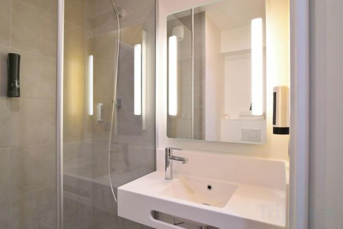 Un baño moderno con cabina de ducha de vidrio, un lavamanos blanco y un espejo grande.