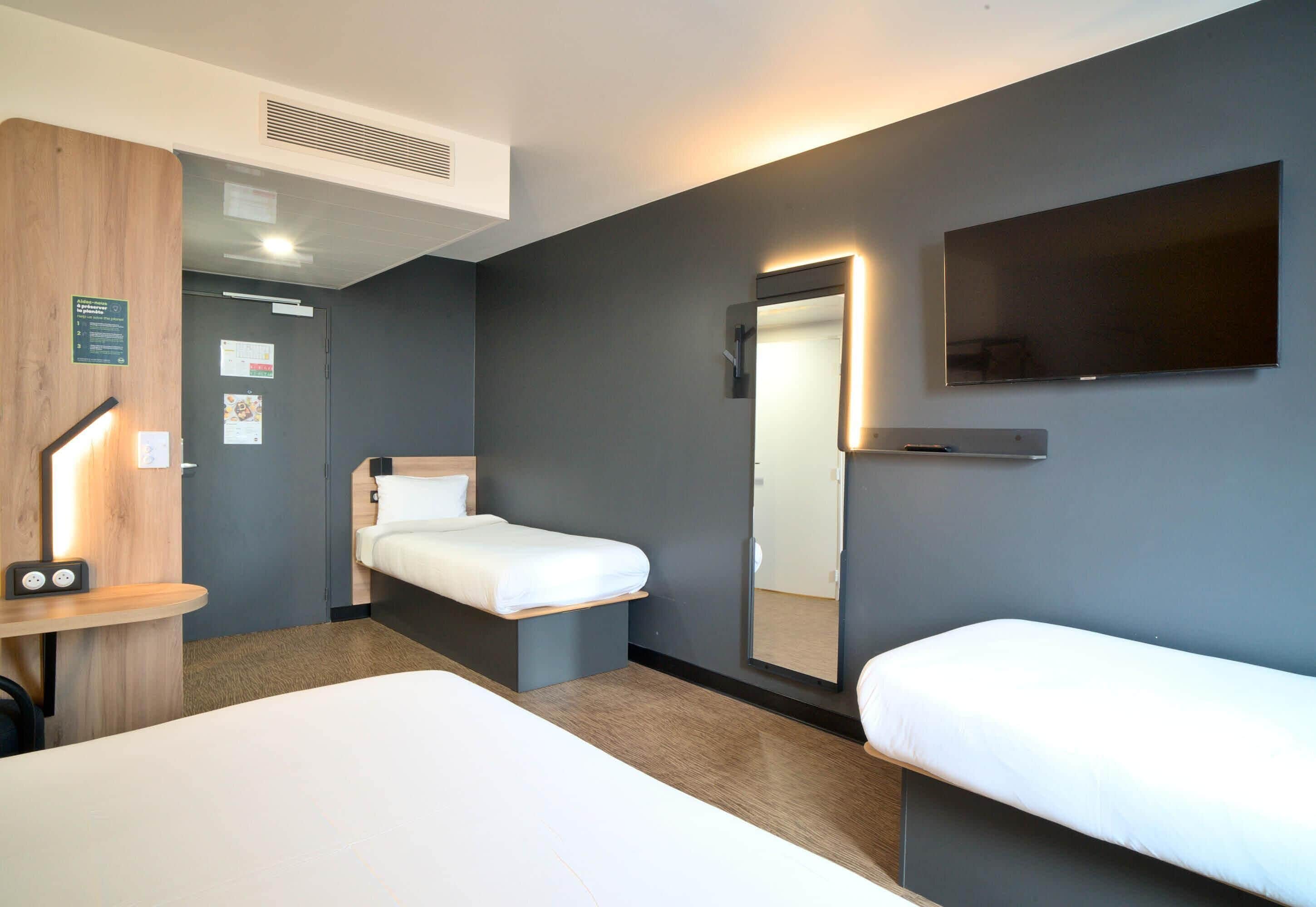 Una habitación de hotel con una cama, un escritorio con una silla, un espejo y un televisor.