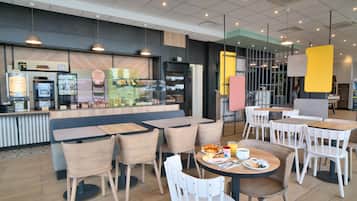 Un café moderne avec des tables et des chaises, un comptoir où l’on sert des boissons et un menu bien visible.