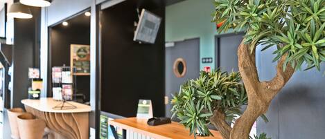 A reception area with a wooden counter, a digital screen, and a potted tree.
