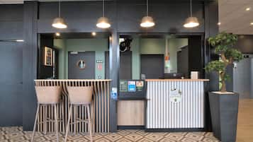Una zona de recepció amb mostrador, dues tamboretes, una planta en test i una pantalla digital d'informació.