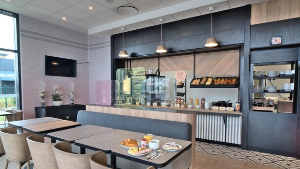 A modern cafe with a counter, seating area, and a variety of food items displayed. - B&B HOTEL Dreux Nord (Dreux)