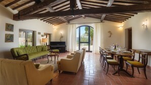 A spacious living area with a green sofa, a piano, and a dining table set for six. - Villa Le Logge 12, Emma Villas (Todi)
