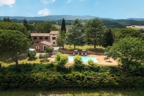 A villa with a swimming pool, surrounded by lush greenery and hills in the background.