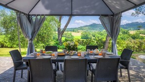 An outdoor dining area with a table set for six, surrounded by wicker chairs, under a canopy with curtains. - Fonte Pinella 8, Emma Villas (Chiusi)
