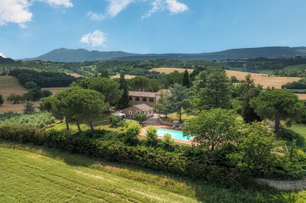A villa with a swimming pool surrounded by lush greenery and fields.