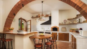 A kitchen with a brick archway, a round wooden table with chairs, and a hanging light fixture. - Fonte Pinella 8, Emma Villas (Chiusi)
