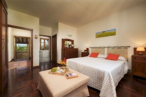 A bedroom with a large bed, a wooden nightstand, a bedside table, a mirror, and a view of the outdoors.