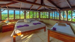 Un dormitorio amplio con una cama grande, una cama más pequeña y un escritorio. La habitación tiene ventanas grandes que ofrecen vistas al exterior.