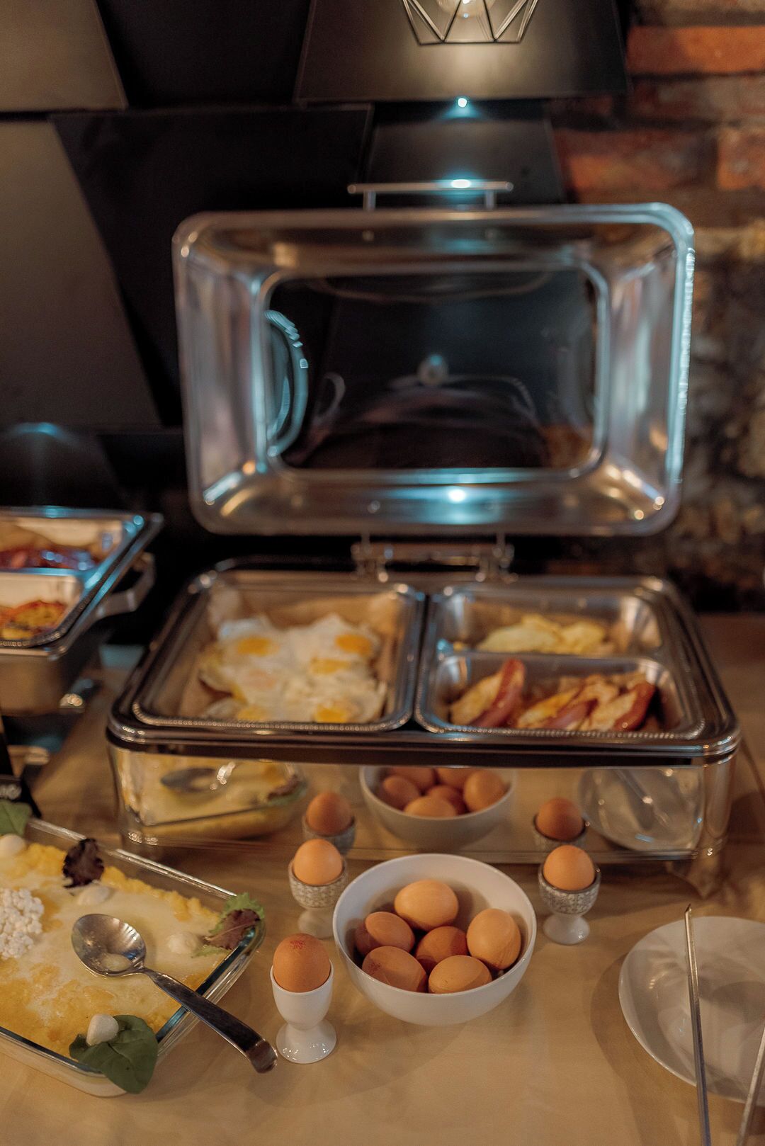A buffet setup with various food items including eggs, bacon, and a casserole dish.