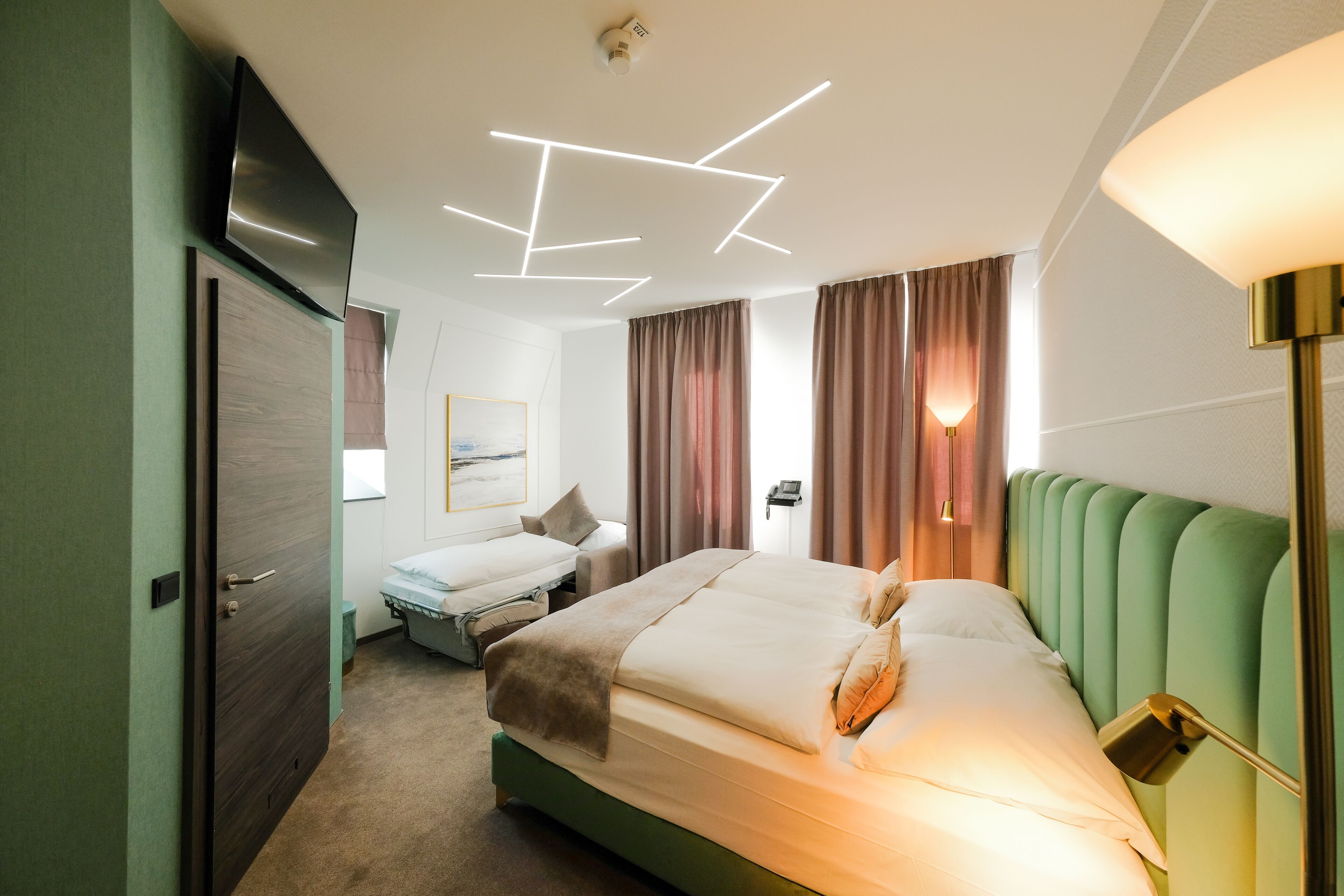 Hotellihuone, jossa on suuri sänky, työpöytä, tuoli, televisio ja moderni kattovalaisin.