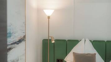 A hotel room with a bed, a green headboard, a floor lamp, and a painting on the wall.