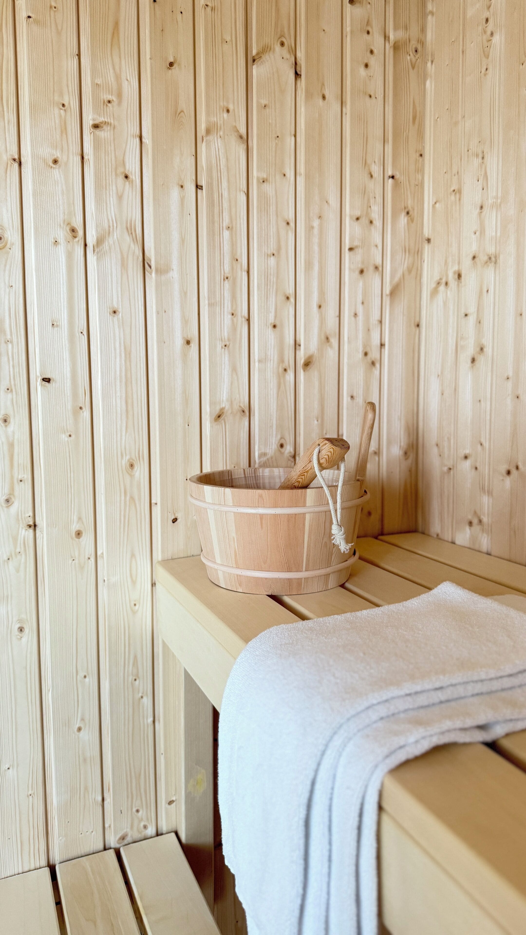 A wooden sauna with a wooden bucket and a towel on a bench.