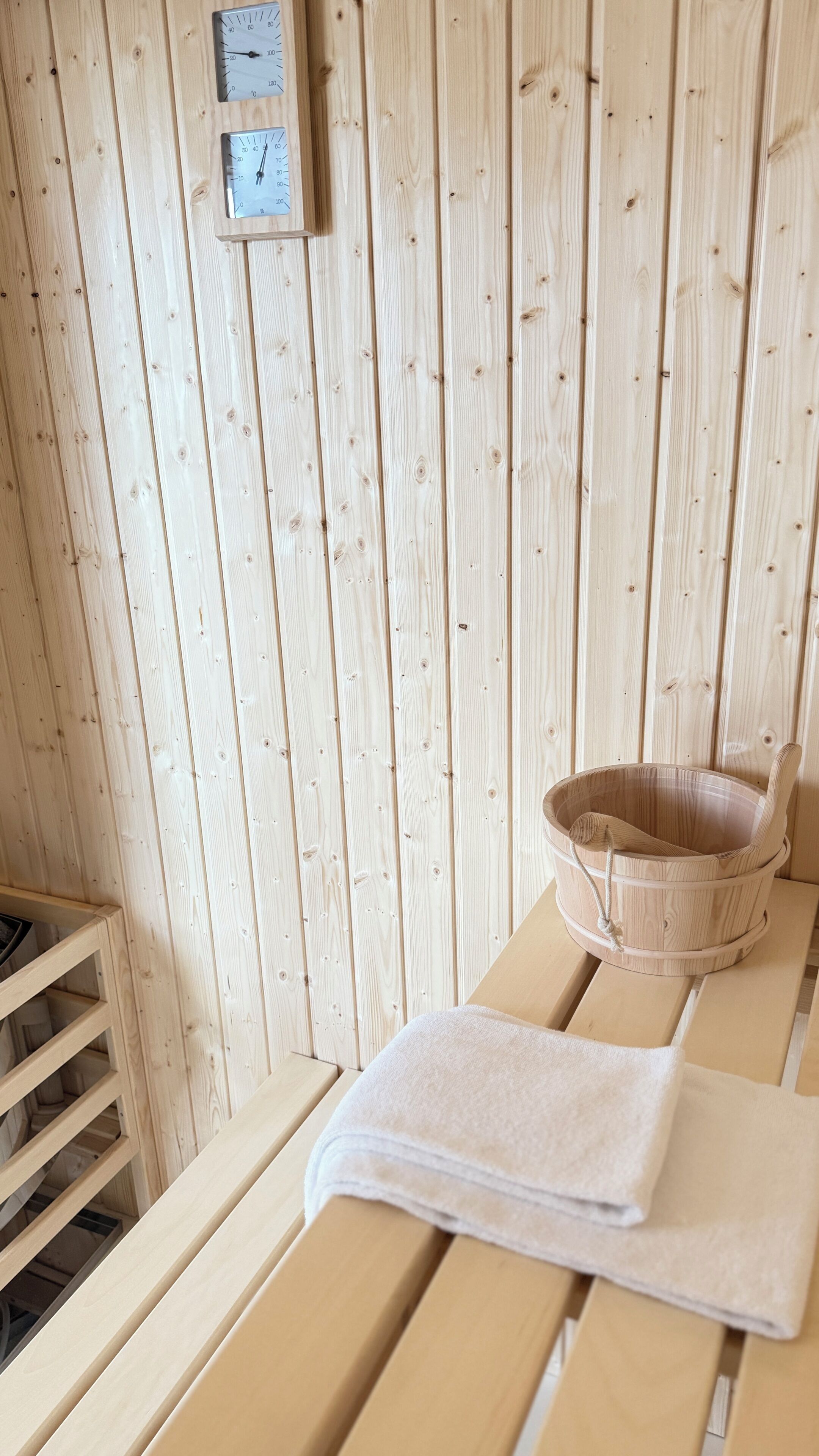 Et saunaområde med trævægge, en bænk, en spand og et håndklæde.