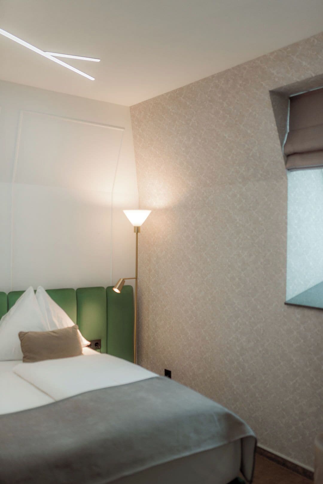 A hotel room with a bed, a nightstand, a lamp, and a window.