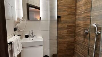 A modern bathroom with a glass shower enclosure, a white vanity with a mirror, and a wooden floor.