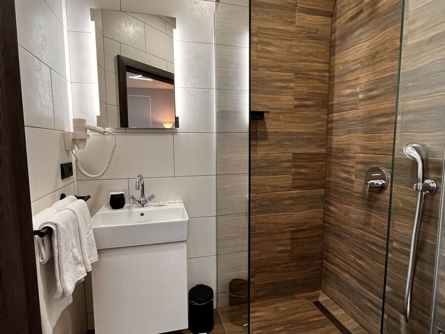 A modern bathroom with a glass shower enclosure, a white vanity with a mirror, and a wooden floor.
