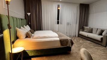 Una habitación de hotel moderna con una cama grande, un cabecero tapizado en verde, un escritorio y un sofá.