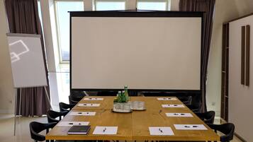 A conference room with a long table, black chairs, a projector screen, and a whiteboard.