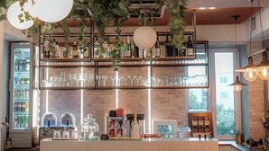 Un espace bar avec un comptoir, des étag ères remplies de bouteilles, de verres et un réfrigérateur. Des lampes sont suspendues au-dessus du bar, et des chaises sont disposées tout autour.