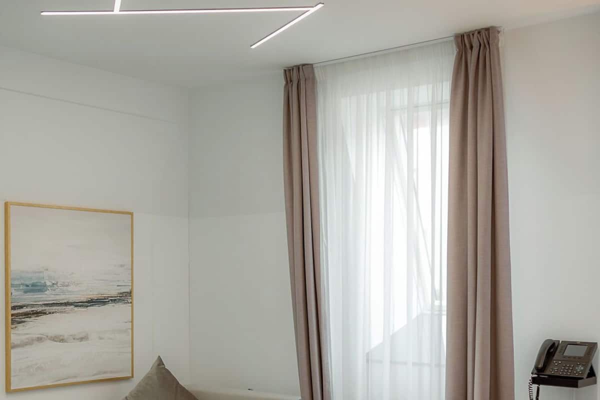 Una habitación de hotel moderna con cama, sofá, un cuadro y teléfono sobre un soporte.