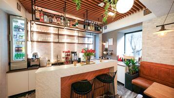 A bar area with a refrigerated display, shelves with bottles, a coffee machine, and seating.