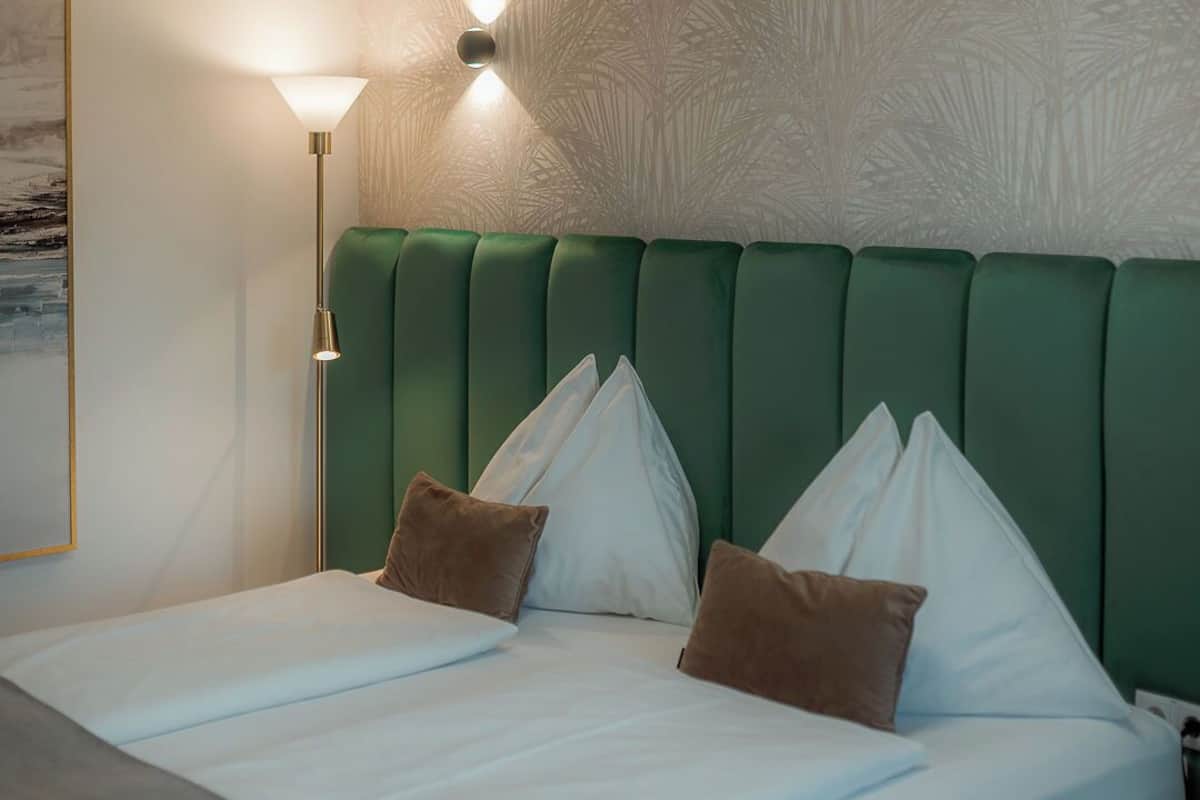 Una habitación de hotel con una cama grande, un cabecero tapizado en verde y una lámpara fijada a la pared.