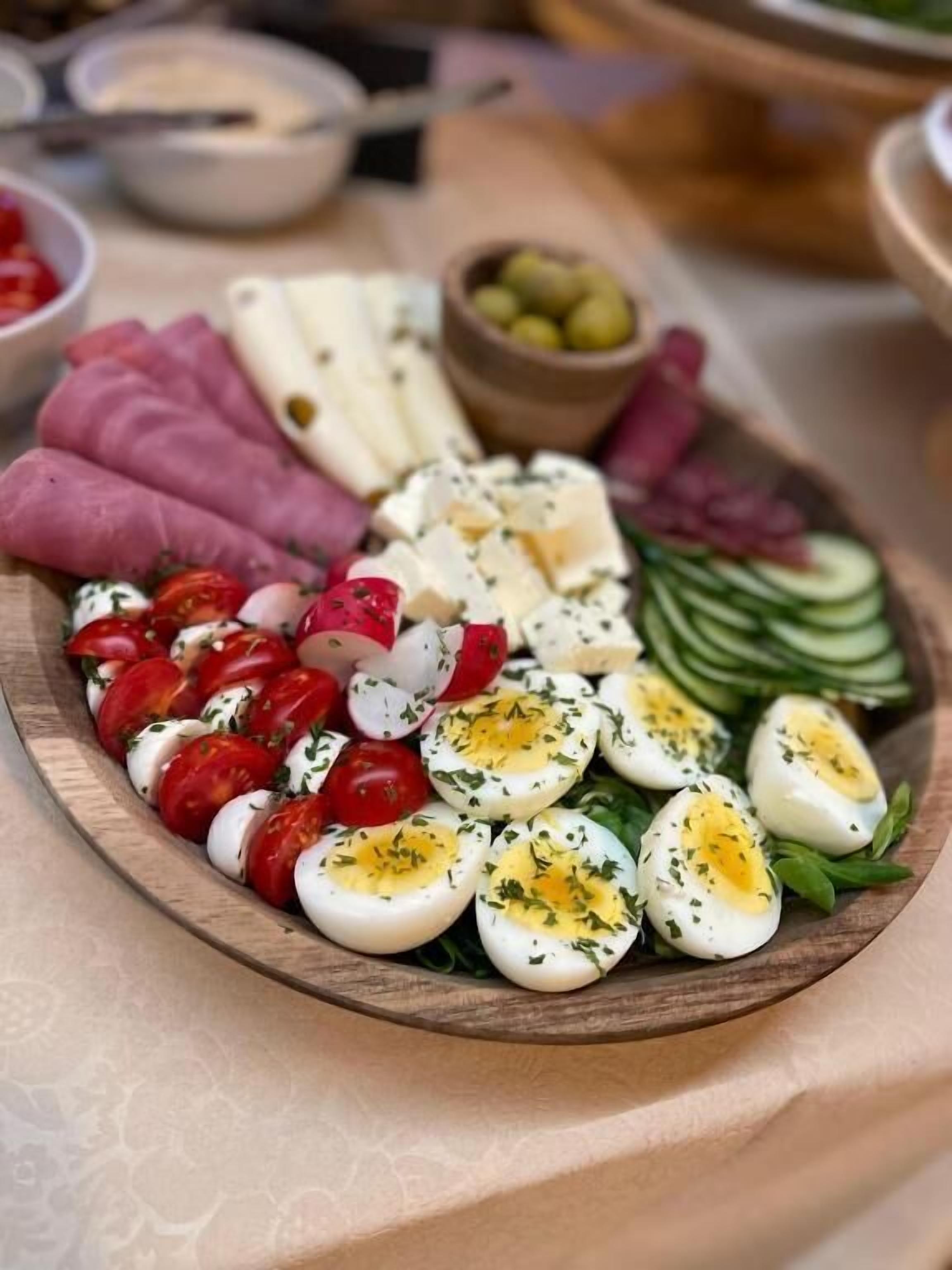 Una tabla de madera con diversos alimentos, entre ellos tomates, queso y pepinos en rodajas.