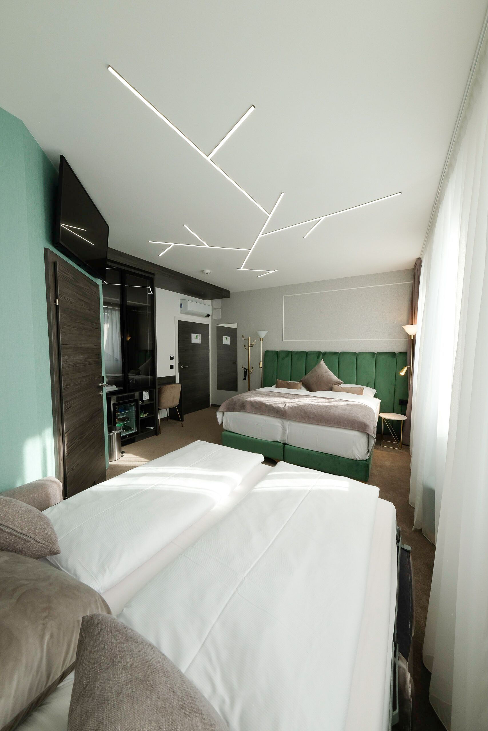 A modern hotel room with two beds, a green headboard, and a built-in TV.