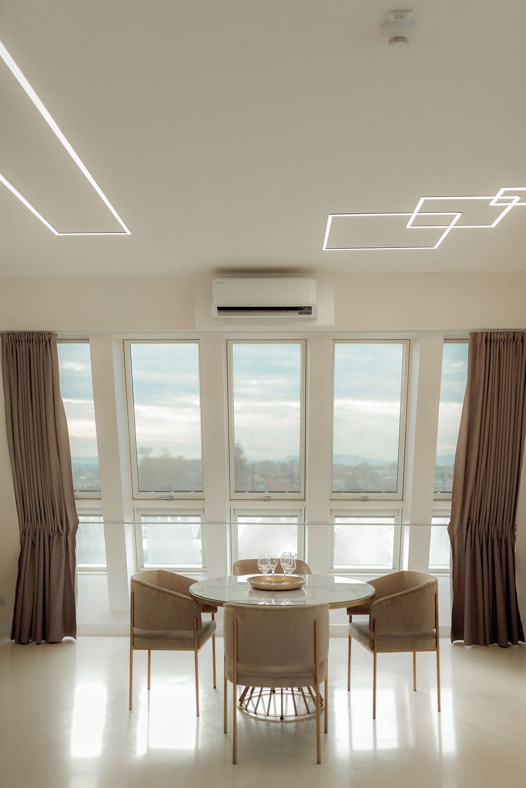 A modern dining room with a round table, four chairs, and a view through large windows.