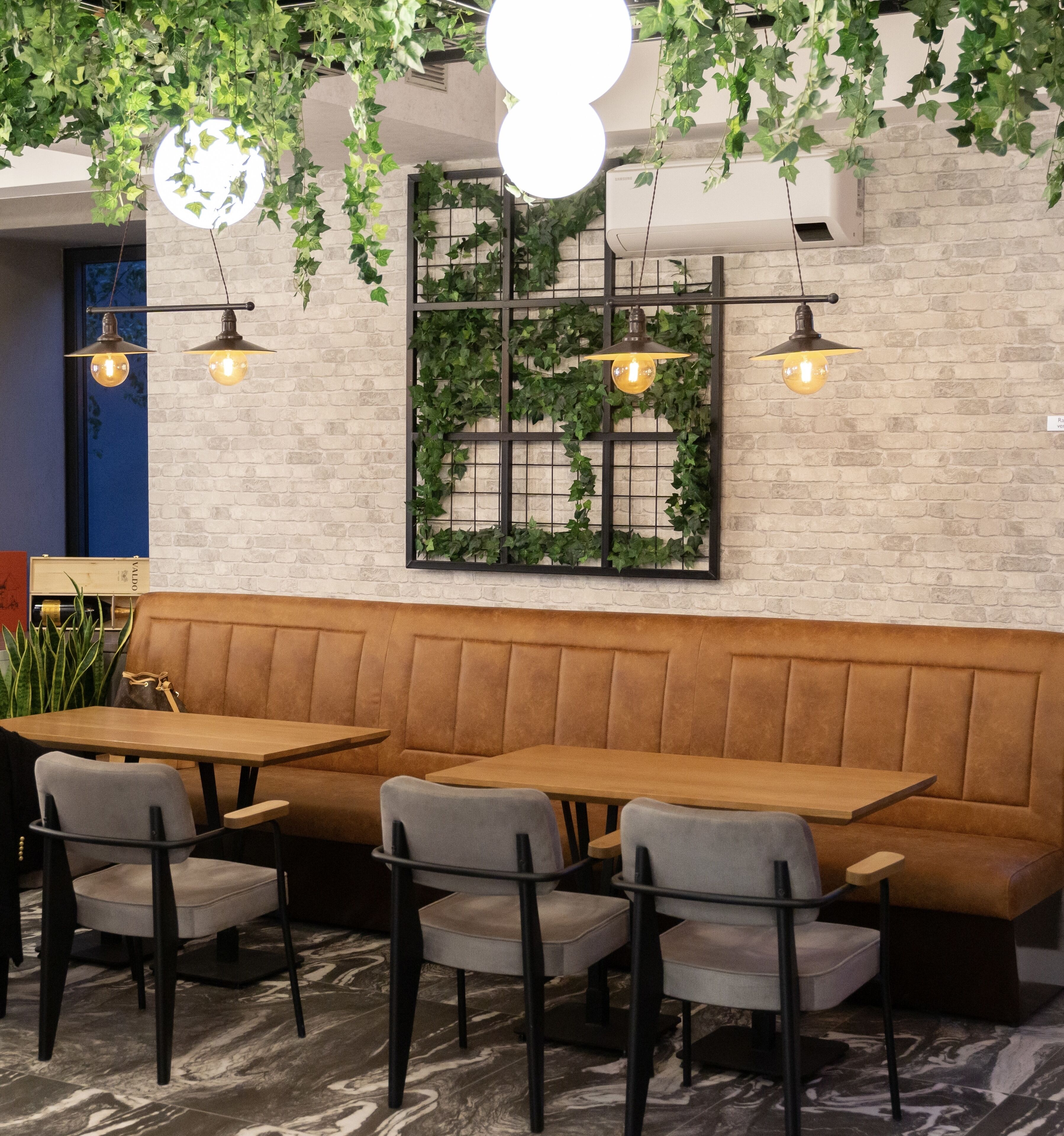 A restaurant interior with a brick wall, green vines, and hanging pendant lights.