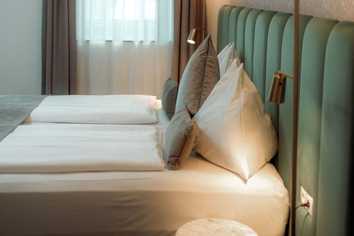 Una habitación de hotel con una cama, una lámpara de noche y un ventanal con cortinas.