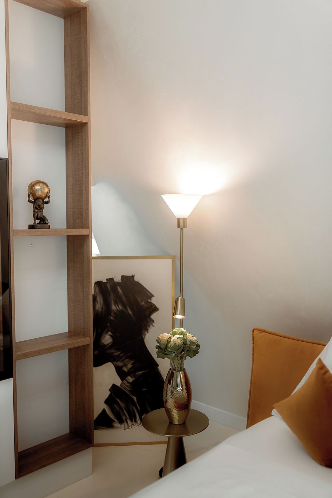 Una habitación con una cama, una mesita de noche con una lámpara, un estante de madera con un globo terráqueo y una obra de arte enmarcada.