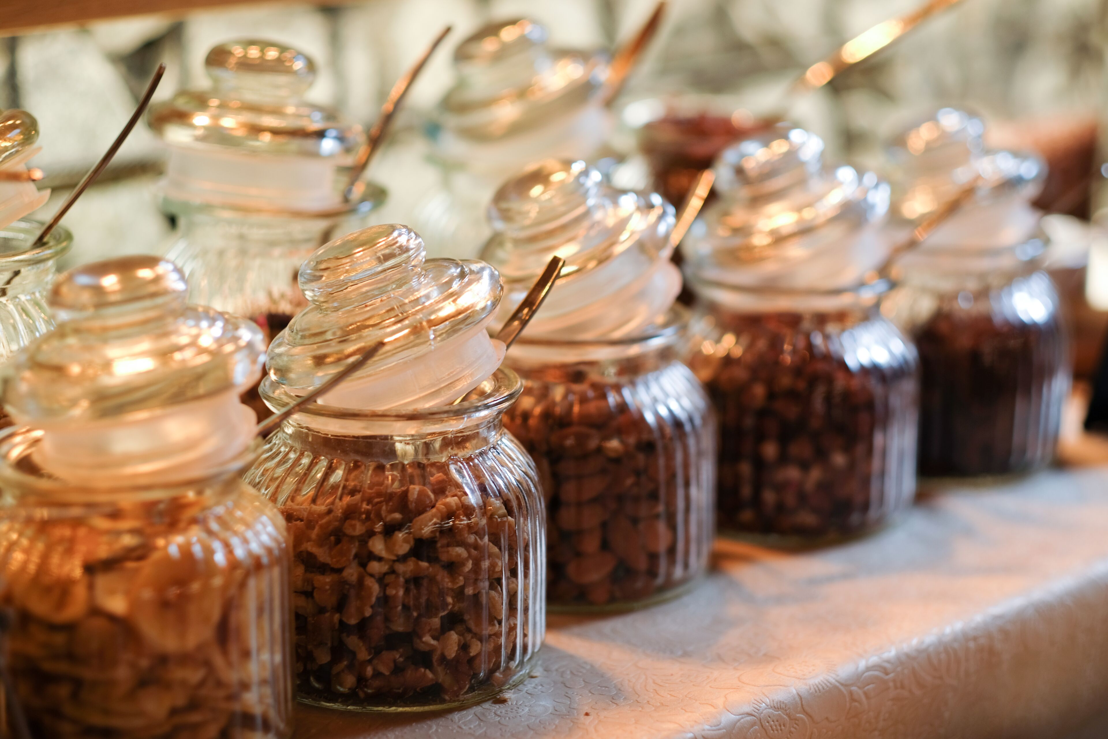 A row of glass jars with metal lids, each containing a different type of food item.
