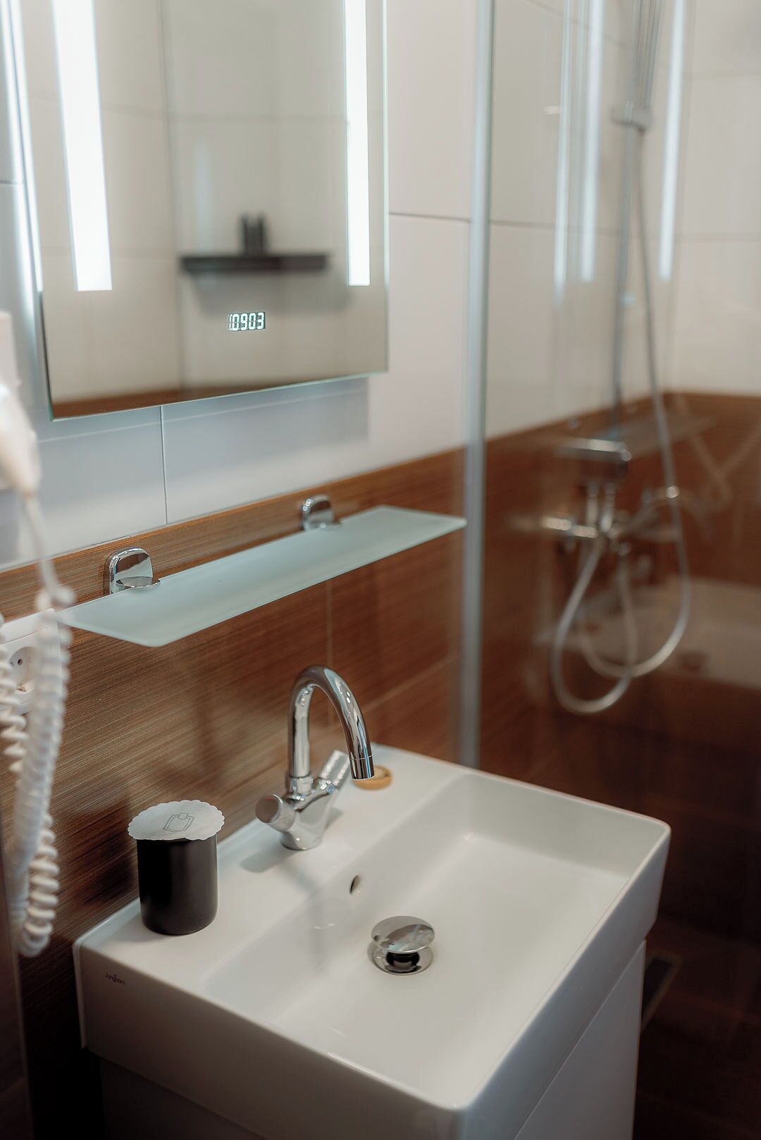 Un baño moderno con un lavamanos blanco, un espejo encima y una zona de ducha visible a través de un panel de vidrio.