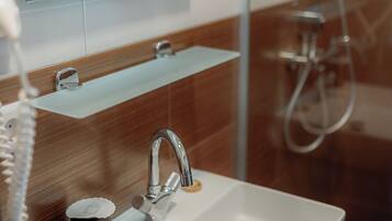 A modern bathroom with a white sink, a mirror above it, and a shower area visible through a glass partition.