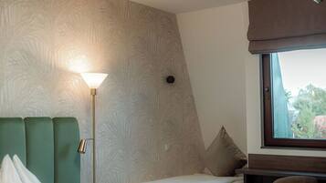 A hotel room with a bed, a desk, and a chair. There is a window with a view of trees.