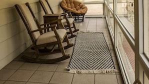 Une véranda couverte avec un ventilateur de plafond, des fauteuils à bascule en bois et une vue sur un paysage montagneux grâce à de grandes fenêtres.