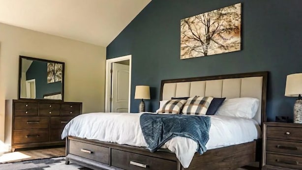 Une chambre avec un grand lit, une commode en bois foncé et un tableau accroché au mur.
