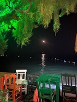 Vista noturna de um restaurante à beira-mar com mesas ao ar livre e vista para a água.