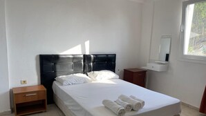 A neatly made bed with white linens and rolled towels, a wooden nightstand, a small wooden cabinet, and a window with a view of trees. - Ayci Otel (Bodrum)