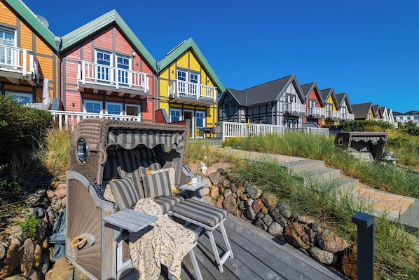 A row of colorful houses with balconies, a wooden deck with outdoor furniture, and a stone wall.