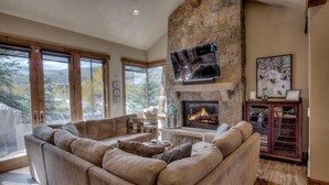 A spacious living room with a stone fireplace, large windows, and a comfortable seating area. - Happy Place | Private Hot Tub • 3 King Suites • Minutes to Breck Ski Resort (Breckenridge)