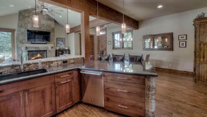 A spacious kitchen with a stone fireplace, wooden cabinets, and a large island. - Happy Place | Private Hot Tub • 3 King Suites • Minutes to Breck Ski Resort (Breckenridge)