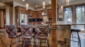 A modern kitchen with wooden cabinets, a central island with bar stools, and pendant lighting. - Happy Place | Private Hot Tub • 3 King Suites • Minutes to Breck Ski Resort (Breckenridge)