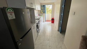 Eine schmale Küche mit weißen Schränken, einem Edelstahlkühlschrank und einem Fliesenboden.