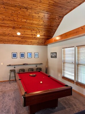 A pool table with a red felt surface, surrounded by chairs and a billiards rack.